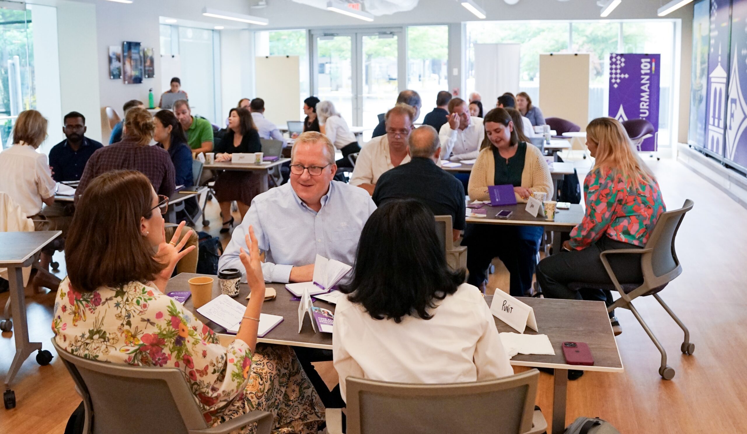 A large group of professionals in groups of three and four at various tables throughout the room.